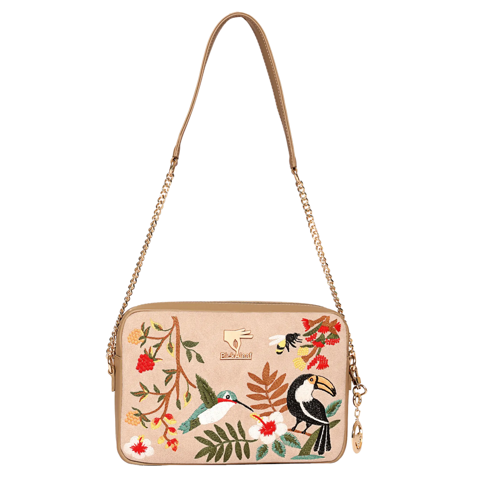 Mystic Garden Crossbody Bag by PickALeaf in beige vegan leather, with a gold-tone chain strap and tropical toucan, hummingbird and floral embroidery.